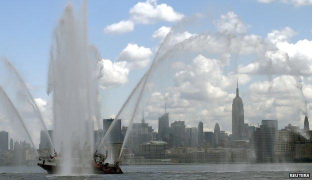 The New York City skyline and the Empire State Building are visible under the spray from a fire boat