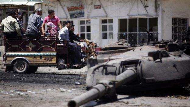 Syrians look at a destroyed military tank