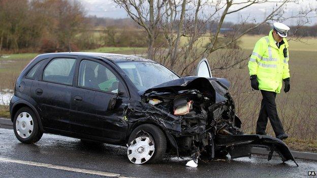 Policeman walks past crashed car by side of the road