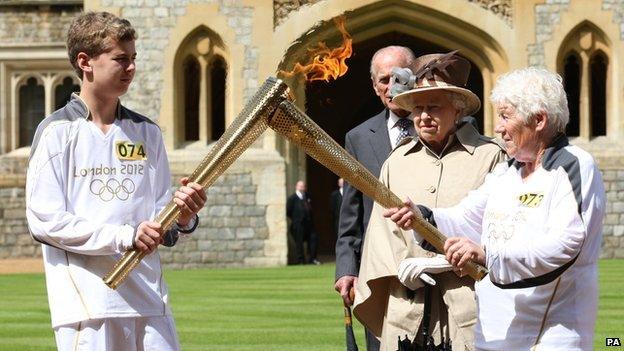 Queen watches as two people pass on the Olympic flame