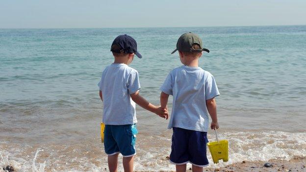 Twins hold hands on the edge of the sea.