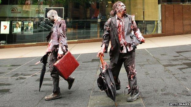 Two men dressed as zombie business men walk down a street