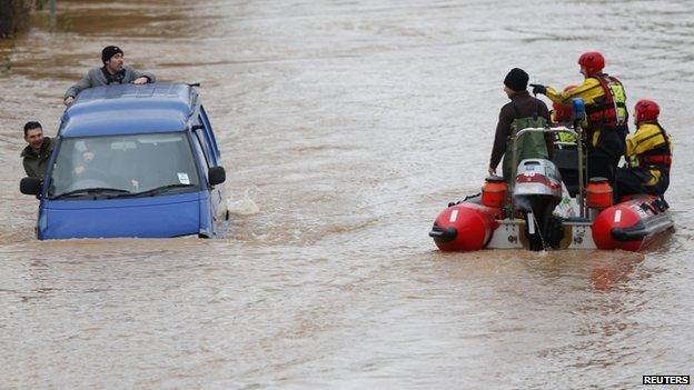 Rescue crews in a dingy pass a van driving along a flooded street in Gloucester