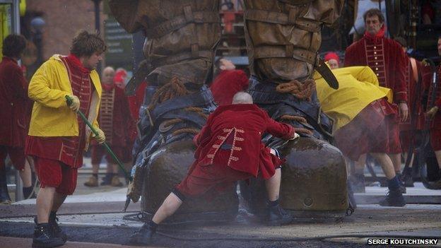 Several men work the feet of a giant marionette