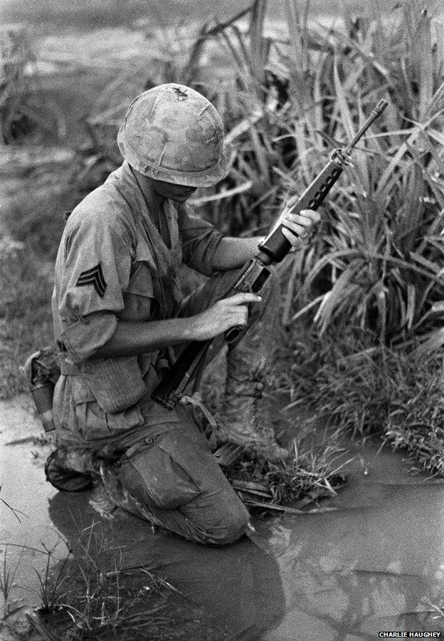 A Sergeant kneels on wet ground and checks his M16