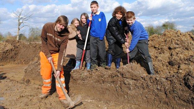 Children and a workman digging on a patch of mud