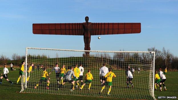 Boys play football in the shadow of the Angel of the North near Gateshead