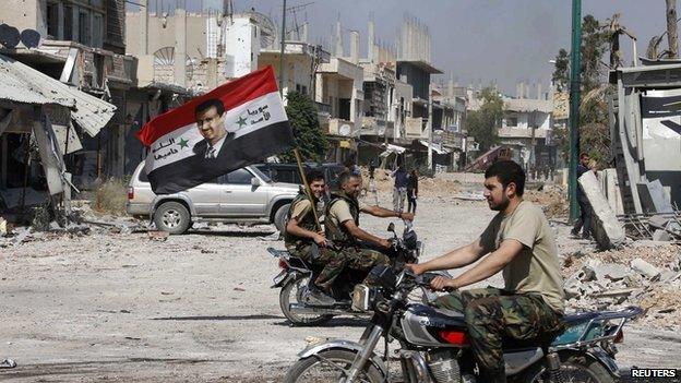 Forces loyal to President Bashar al-Assad carry the national flag as they ride on motorcycles in Qusair, after the Syrian army took control from rebel fighters, June 5, 2013.