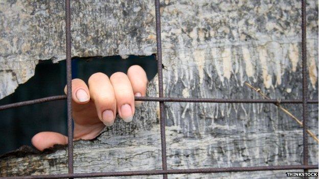 A hand of someone kept in solitary confinement showing through a crack in a wooden board