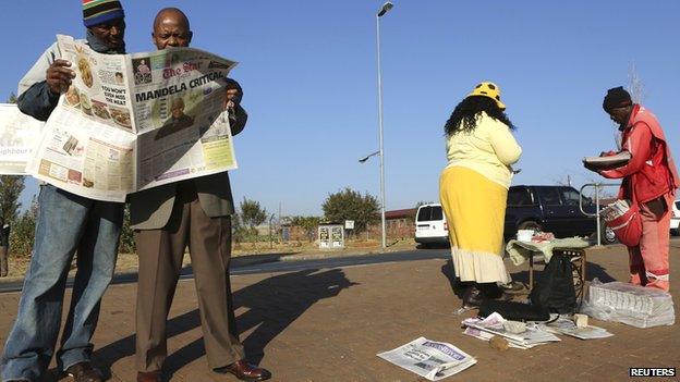 Men read a newspaper next to a stall in Soweto on 24 June 2013