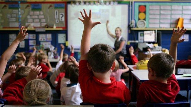 Children with their hands up in a classroom