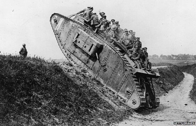 British troops riding on the back of the Mark IV tank as it crawls over a trench ledge in 1918