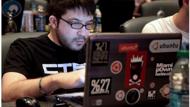 A man behind a computer covered in stickers