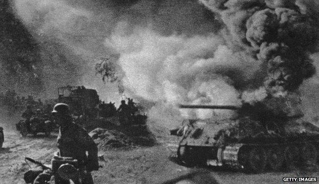 Russian soldiers walk past a burning T-34 tank