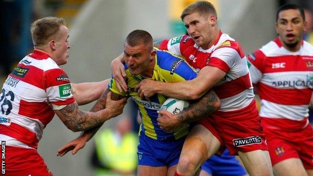 Warrington's Paul Wood is tackled by Wigan's Sam Tomkins and Dom Crosby