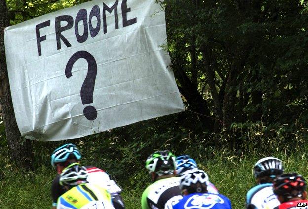 Riders go past a sign saying 'Froome?'