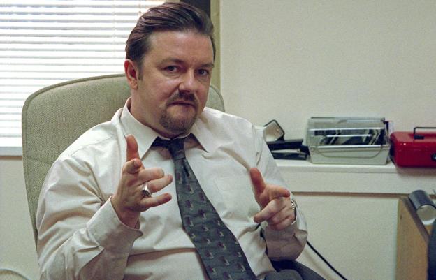 Ricky Gervais as David Brent in The Office, sat behind his desk pointing at the camera with both hands