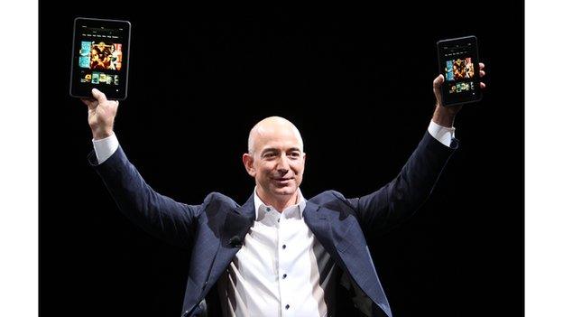 Jeffrey Bezos, the founder of Amazon, holds up electronic products