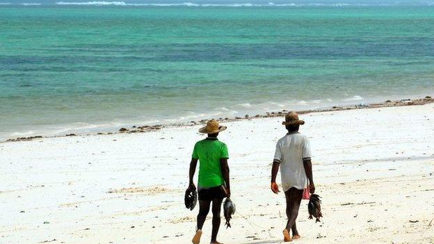 People walk along a beach in Zanzibar carrying fish