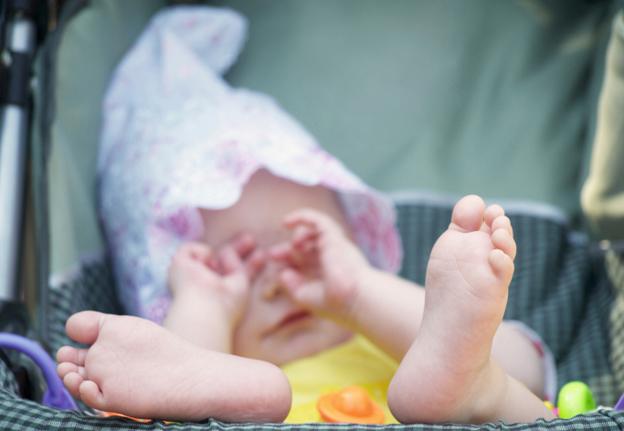 A baby in a pram, wiping her eyes with her hands