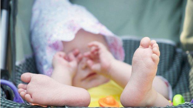 A baby in a pram, wiping her eyes with her hands