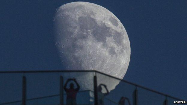 Visitors stand on the roof of a skyscraper as the moon rises over the skyline of Lujiazui financial district of Pudong in Shanghai 16 August, 2013