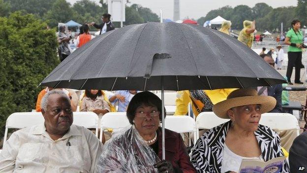 Three people wait under an umbrella in front of the Lincoln Memorial, Washington DC on 28 August 2013