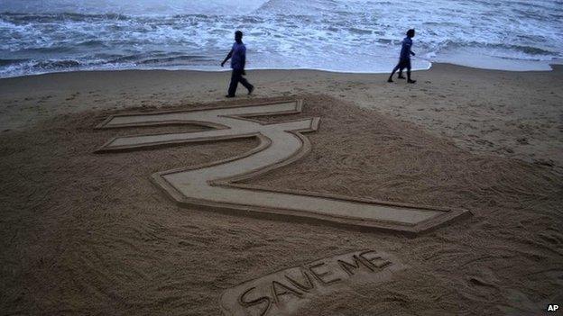 Visitors walk past a sand sculpture depicting the Indian Rupee by sand artist Sudarshan Pattnaik on the Bay of Bengal coast at Puri, Orissa state, India, Tuesday, Aug.27, 2013.