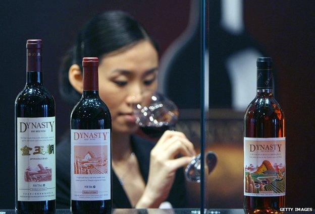 A shelf of Chinese wine, with woman tasting in background