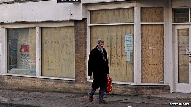 A man walks past some boarded up shops