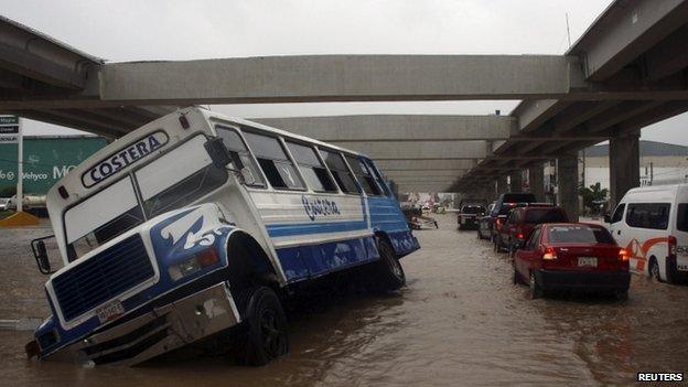 A stranded bus is seen as cars make their way through a flooded street in Acapulco on 15 September, 2013