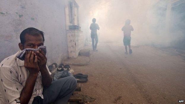 An Indian man covers his face as children follow a municipal corporation worker fumigating the area to prevent mosquitoes from breeding in New Delhi on September 27, 2013