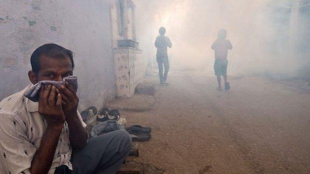 An Indian man covers his face as children follow a municipal corporation worker fumigating the area to prevent mosquitos from breeding in New Delhi on September 27, 2013