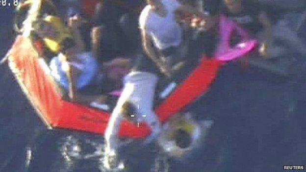 Migrants climb aboard a life raft deployed by an Armed Forces