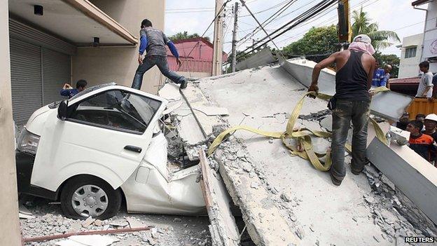Workers use a crane to lift up concrete block that fell on a car after buildings collapsed during an earthquake in Cebu city, central Philippines, 15 October 2013