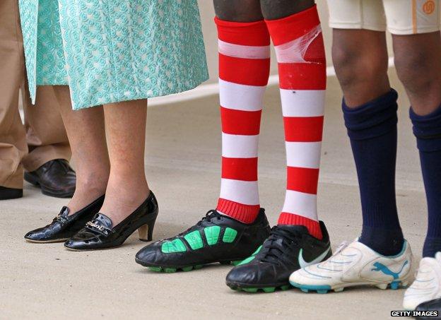 The Queen and two footballers stand