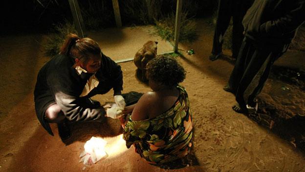 Ros Forester (L) of Tangentyere council night patrol assists an intoxicated Aboriginal woman who had been stabbed during a domestic dispute in a town camp outside the central Australian town of Alice Springs in this picture taken July 5, 2007