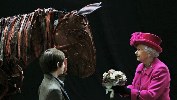 Queen Elizabeth II receives flowers from a child actor as she inspects the horse prop from the theatre production "War Horse" during a visit at the National Theatre in London, Tuesday Oct. 22, 2013 to commemorate the institution’s 50th anniversary