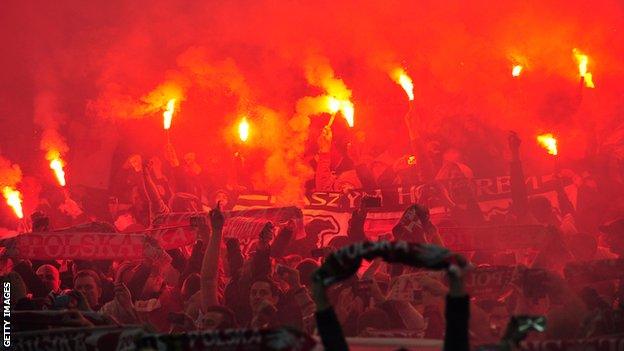 Football supporters hold lit flares aloft as others enjoy the atmosphere outside Wembley Stadium