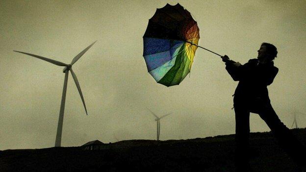 Man with inverted umbrella by wind turbine in storm