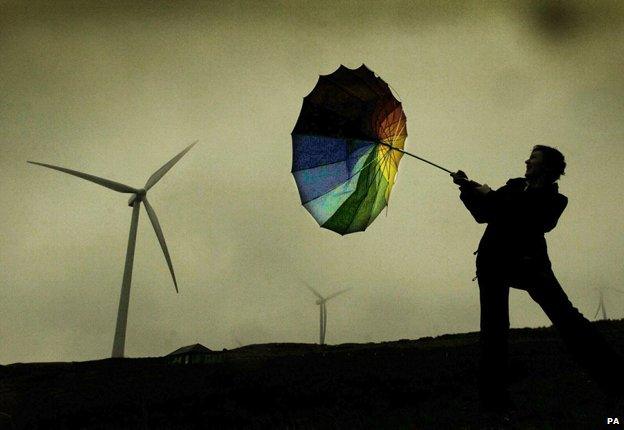 Man with inverted umbrella by wind turbine in storm