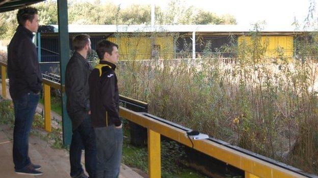 Three fans stand in Meadow Park - Gloucester City's home