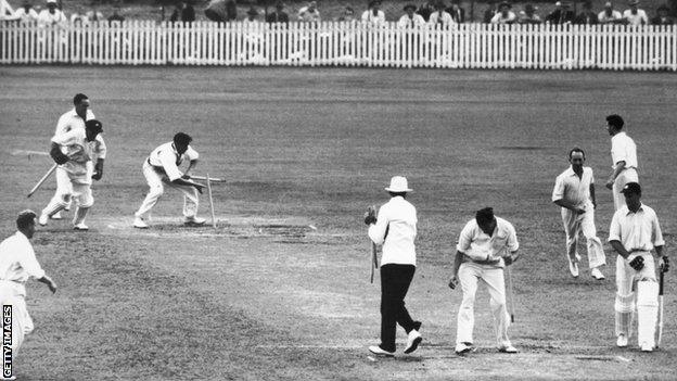 Wicketkeeper Don Tallon gathers up the stumps after Australia win