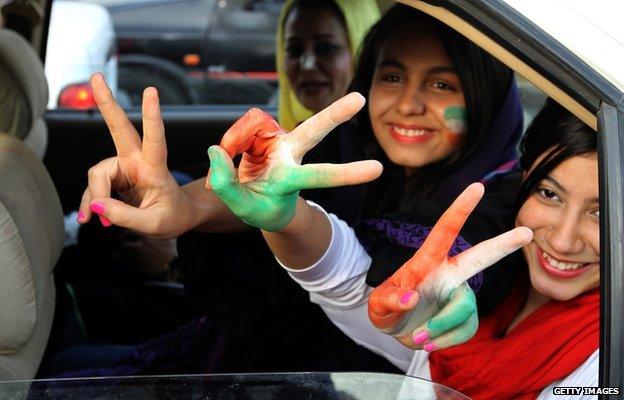 Three Iranian women football supporters in a car with their hands and faces painted in the colours of Iran's flag