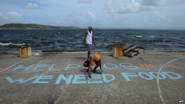 A man paints a message reading "Help SOS We Need Food" at Anibong in Tacloban, eastern island of Leyte (11 November 2013)