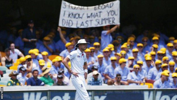 Stuart Broad fields while Australian fans hold up a banner behind him