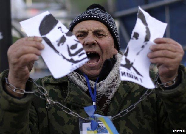 A protester in Kiev, with symbolically chained hands, rips up a picture of Ukrainian President Viktor Yanukovych, 29 November