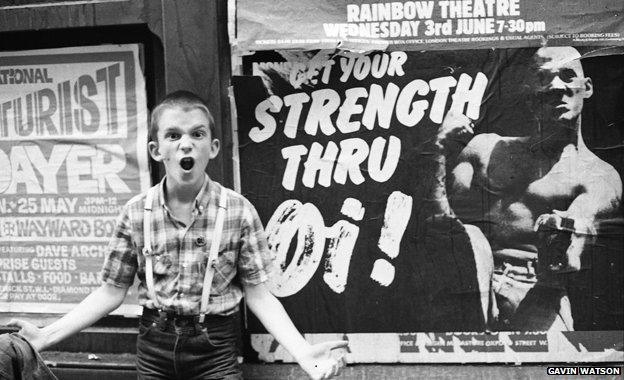 Photographer Gavin Watson's brother stands in front of a "Strength thru Oi!" poster featuring Nicky Crane