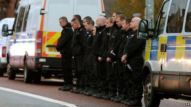 Police officers line the street as the wreckage is taken away