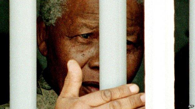 South African President Nelson Mandela stands on 27 March 1998 behind the bars of the former cell where he spent 18 years as a political prisoner on Robben Island